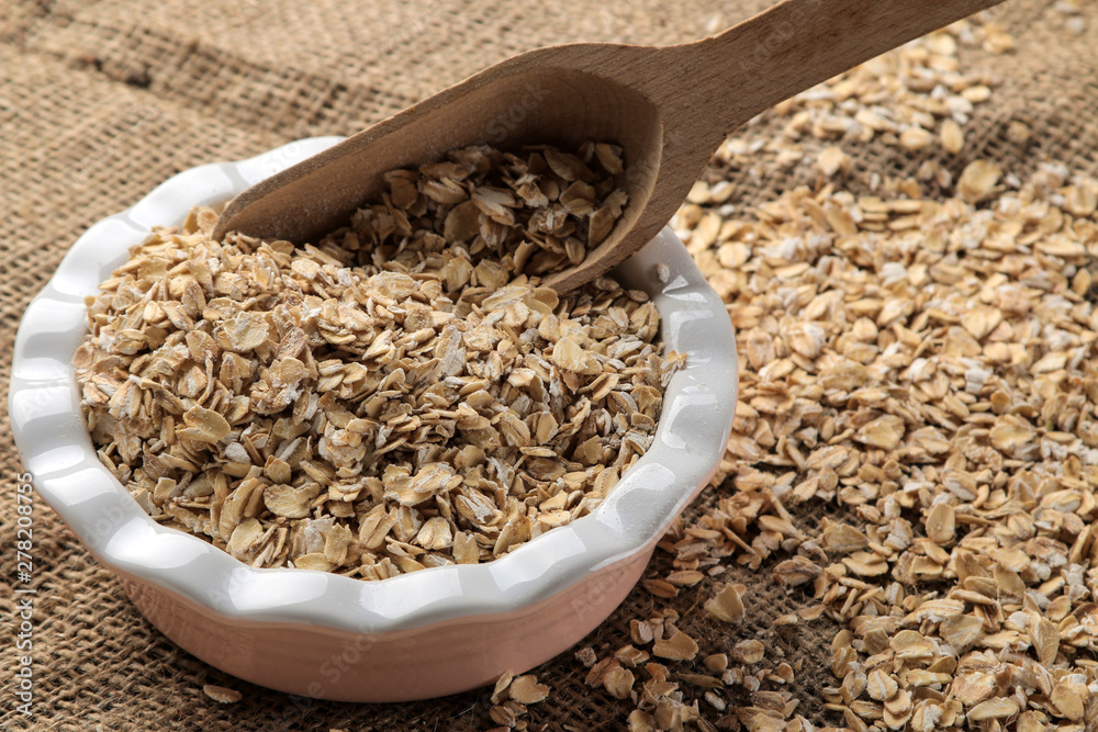 Dry oatmeal flakes in a bowl and a wooden spoon on a brown wooden table. healthy nutrition. healthy food. Dry oatmeal flakes in a bowl and a wooden spoon on a brown wooden table. healthy nutrition. healthy food.