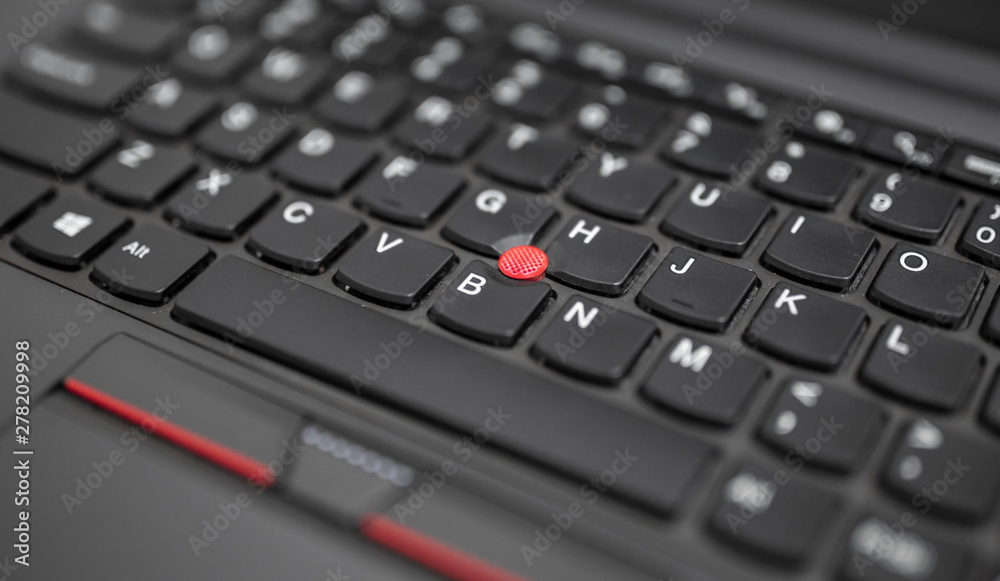 Black laptop keyboard red trackpoint center button cap and touchpad close up view