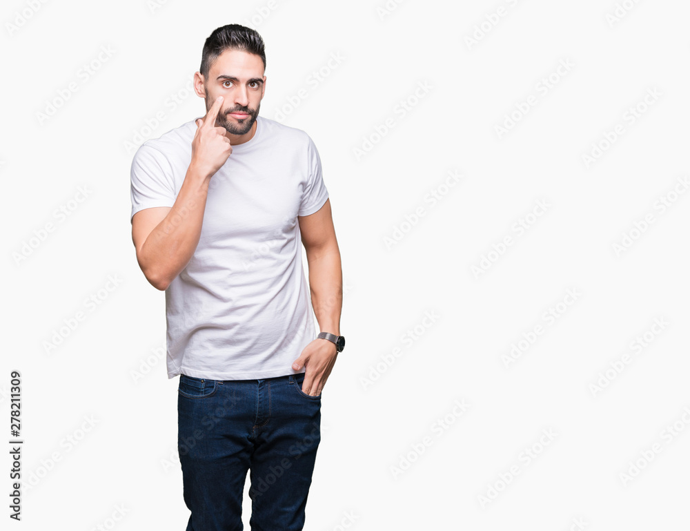 Fototapeta premium Handsome man wearing white t-shirt over white isolated background Pointing to the eye watching you gesture, suspicious expression