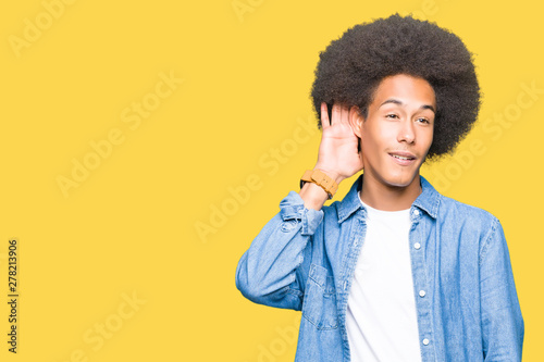 Young african american man with afro hair smiling with hand over ear listening an hearing to rumor or gossip. Deafness concept.