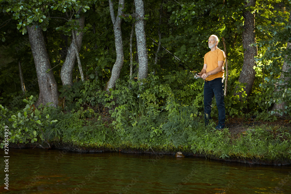 Summer portrait of skilled experienced amateur mature fisherman in casual  clothes and sneakers holding fishing steadily while catching fish in  freshwater of mountain river, standing on bank Stock-Foto | Adobe Stock