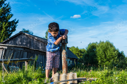 boy in the village in the summer pumping water from the column