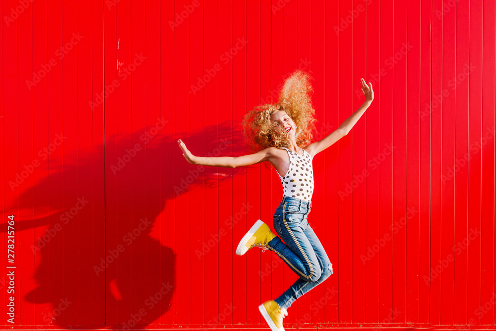 beautiful teen girl makes a jump against the background of a red wall