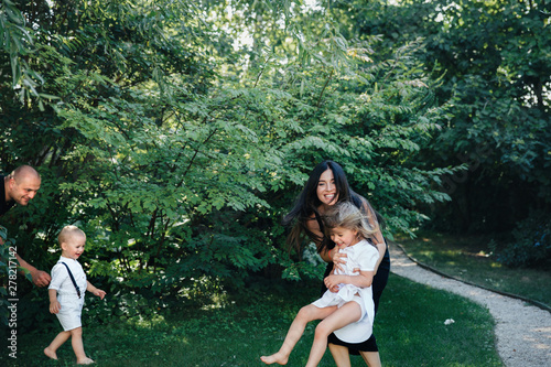 Family of brother and sister in white clothes play with a dad and mom in the park or garden photo