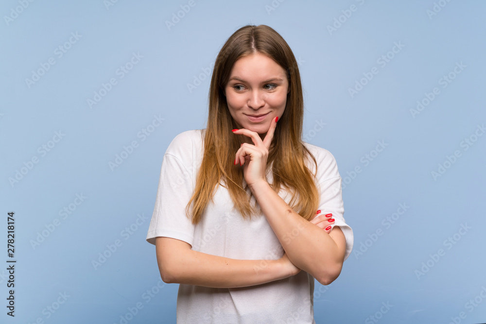 Young woman over blue wall looking down with the hand on the chin Young woman over blue wall looking down with the hand on the chin
