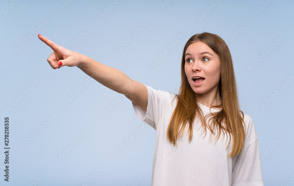 Young woman over blue wall pointing away Young woman over blue wall pointing away