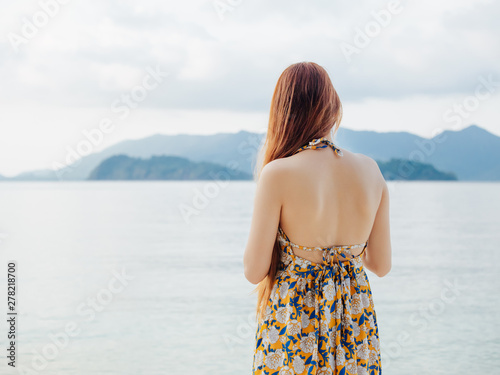 backside of young asian woman relax on beach in summer dress with beautiful skin and smooth, slender body, sea background