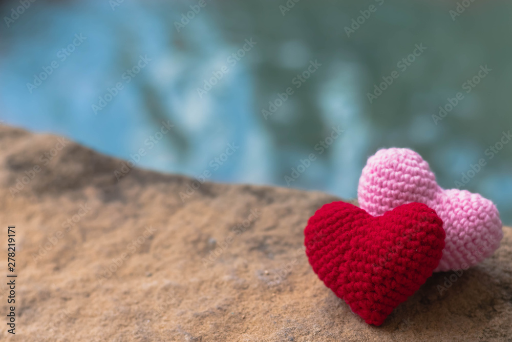 Fototapeta premium Red and pink hearts on stone with beautiful blurred background of waterfall