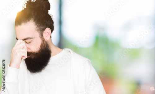 Young man with long hair and beard wearing sporty sweatshirt tired rubbing nose and eyes feeling fatigue and headache. Stress and frustration concept.