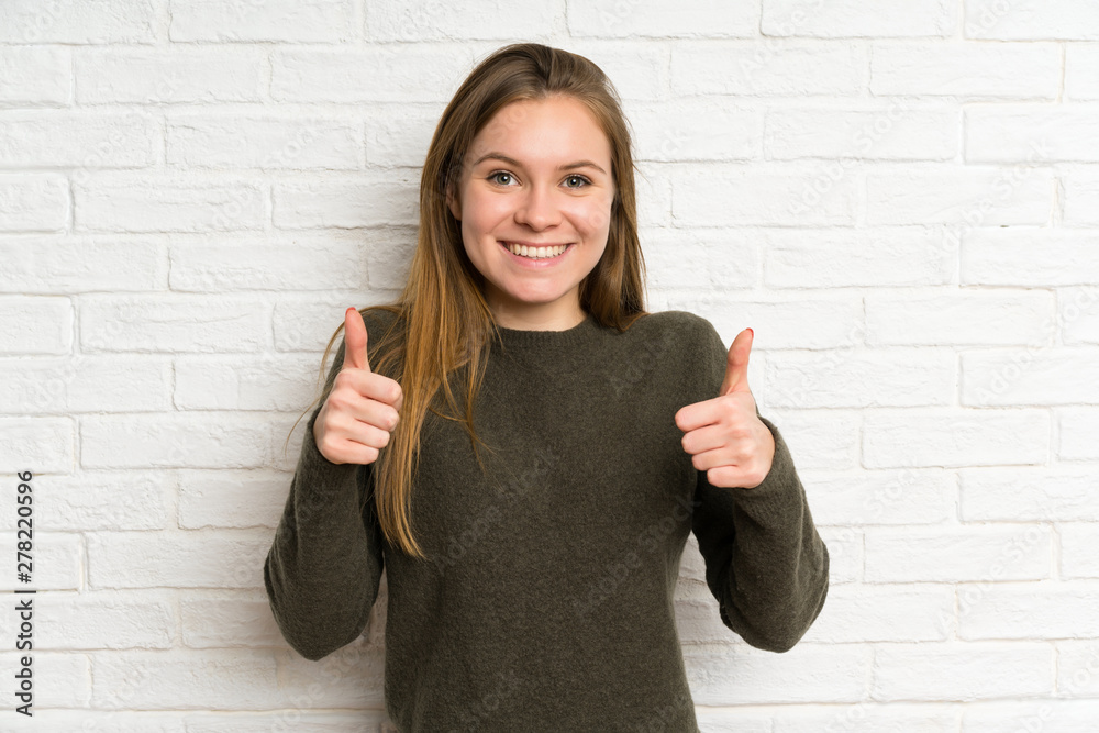 Young woman over white brick wall giving a thumbs up gesture Young woman over white brick wall giving a thumbs up gesture