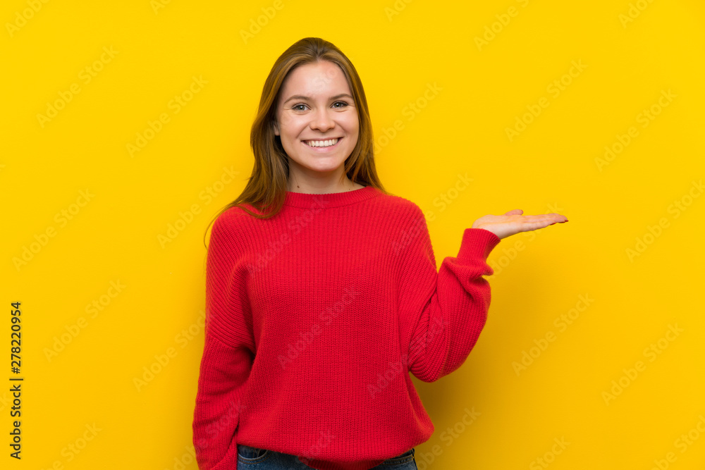 Young woman over yellow wall holding copyspace imaginary on the palm to insert an ad