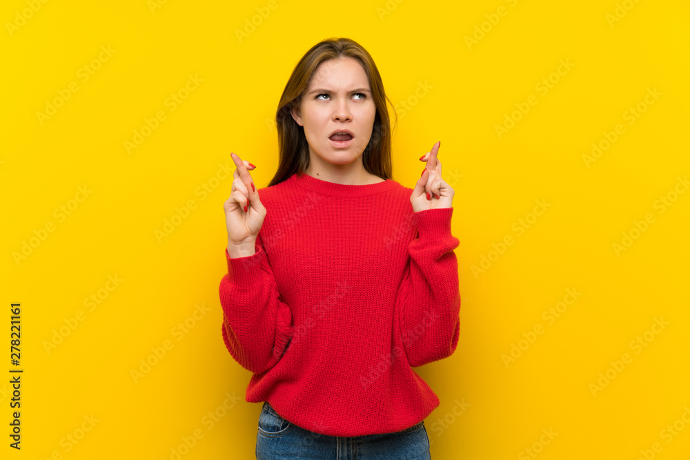 Young woman over yellow wall with fingers crossing and wishing the best Young woman over yellow wall with fingers crossing and wishing the best