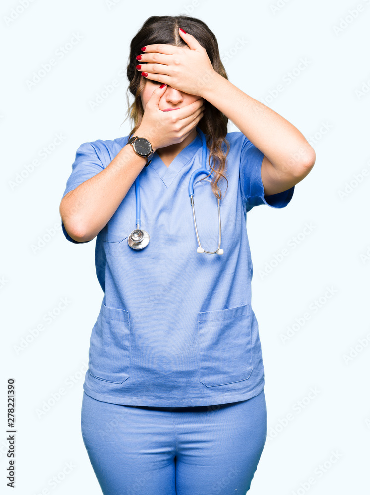 Young adult doctor woman wearing medical uniform Covering eyes and mouth with hands, surprised and shocked. Hiding emotion Young adult doctor woman wearing medical uniform Covering eyes and mouth with hands, surprised and shocked. Hiding emotion