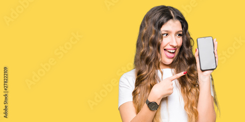 Young adult woman showing smartphone screen very happy pointing with hand and finger