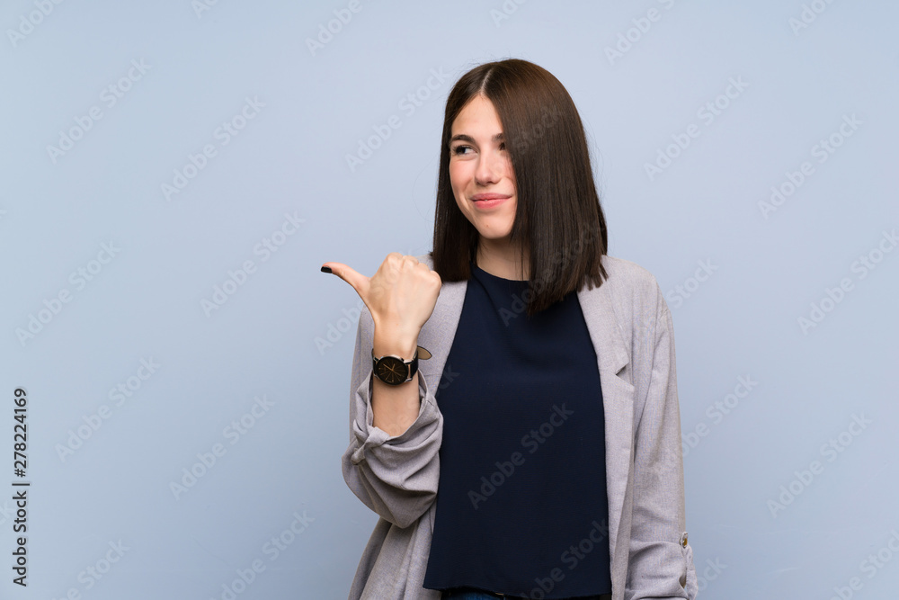Young woman over isolated blue wall pointing to the side to present a product Young woman over isolated blue wall pointing to the side to present a product