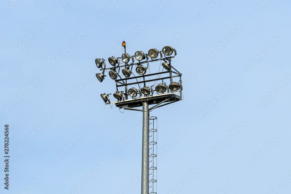 Two lines of stadium light spots or reflectors on a tall tower with clear blue sky in the background