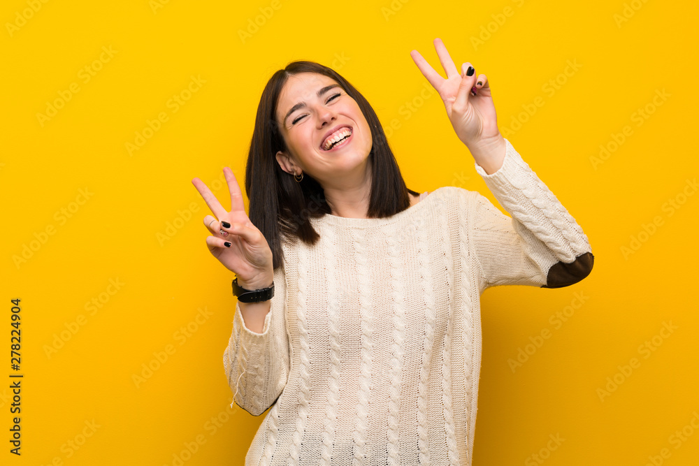 Young woman over isolated yellow wall showing victory sign with both hands