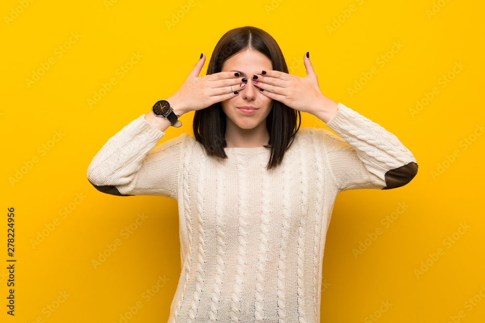 Young woman over isolated yellow wall covering eyes by hands Young woman over isolated yellow wall covering eyes by hands