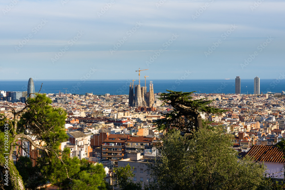 Fototapeta premium View of the roofs of Barcelona from Parc Guell terrace. La Sagrada Familia on the side and the sea on the background. Barcelona.