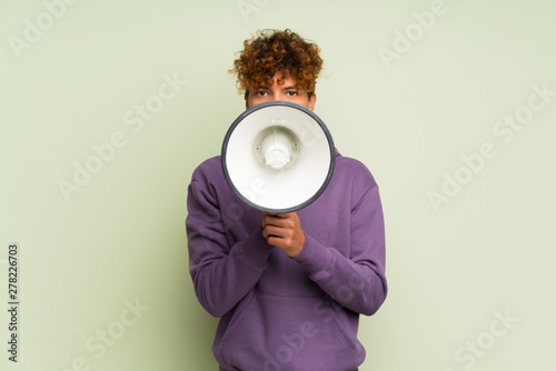 Young african american man over isolated green wall shouting through a megaphone