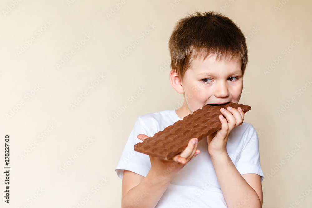 cute five-year-old Caucasian boy in white t-shirt bites big milk chocolate cute five-year-old Caucasian boy in white t-shirt bites big milk chocolate