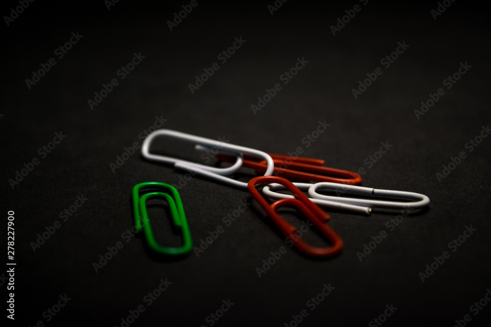 A set of multi-colored office paper clips of plastic are scattered on black monophonic background. A set of multi-colored office paper clips of plastic are scattered on black monophonic background.
