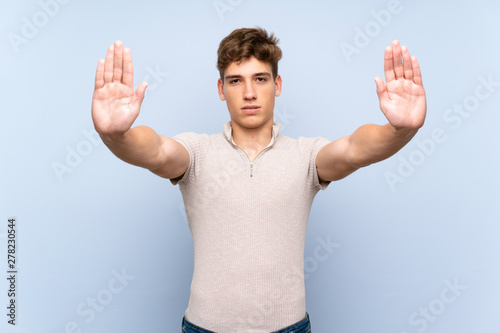 Handsome young man over isolated blue wall making stop gesture and disappointed