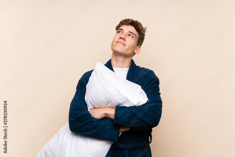 Handsome young man in pajamas over isolated wall looking up while smiling Handsome young man in pajamas over isolated wall looking up while smiling