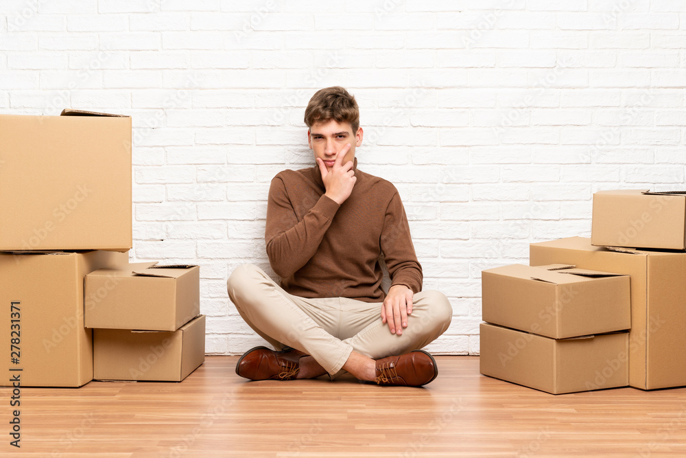 Handsome young man moving in new home among boxes thinking an idea