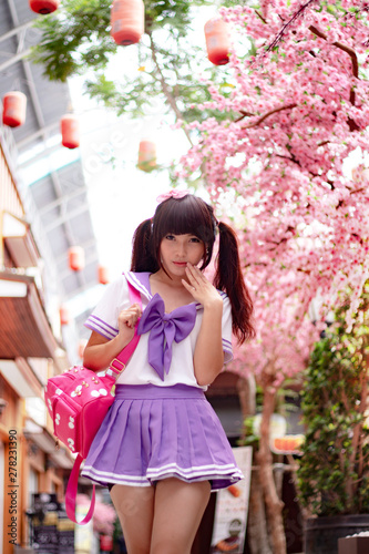 Beautiful Asian model in Japanese student uniform with cherry blossom flower in background