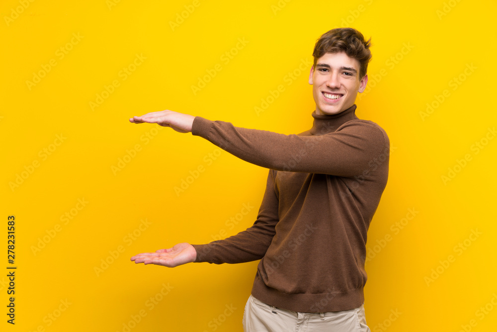 Handsome young man over isolated yellow background holding copyspace to insert an ad
