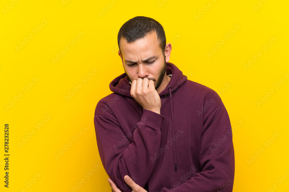 Colombian man with sweatshirt over yellow wall having doubts