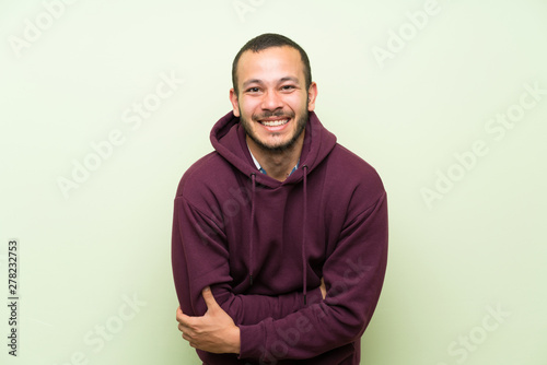 Colombian man with sweatshirt over green wall laughing