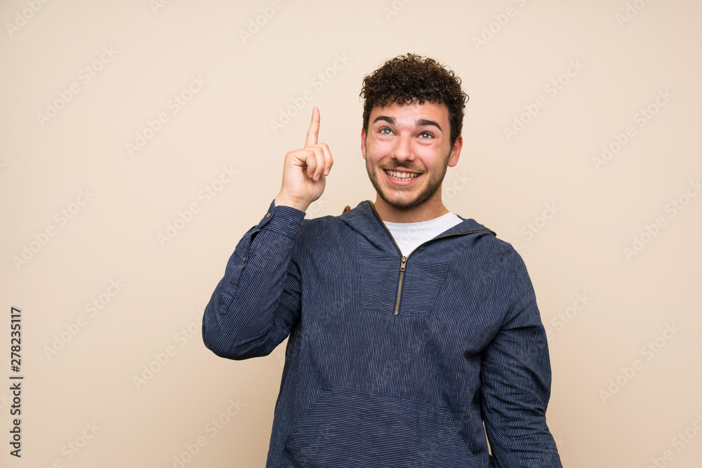 Man with curly hair over isolated wall intending to realizes the solution while lifting a finger up Man with curly hair over isolated wall intending to realizes the solution while lifting a finger up