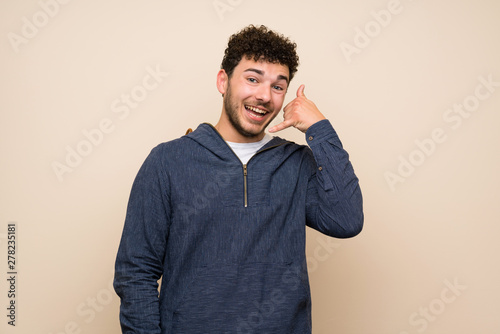 Man with curly hair over isolated wall making phone gesture. Call me back sign