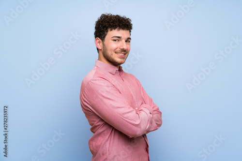 Man with curly hair over isolated blue wall with arms crossed and looking forward