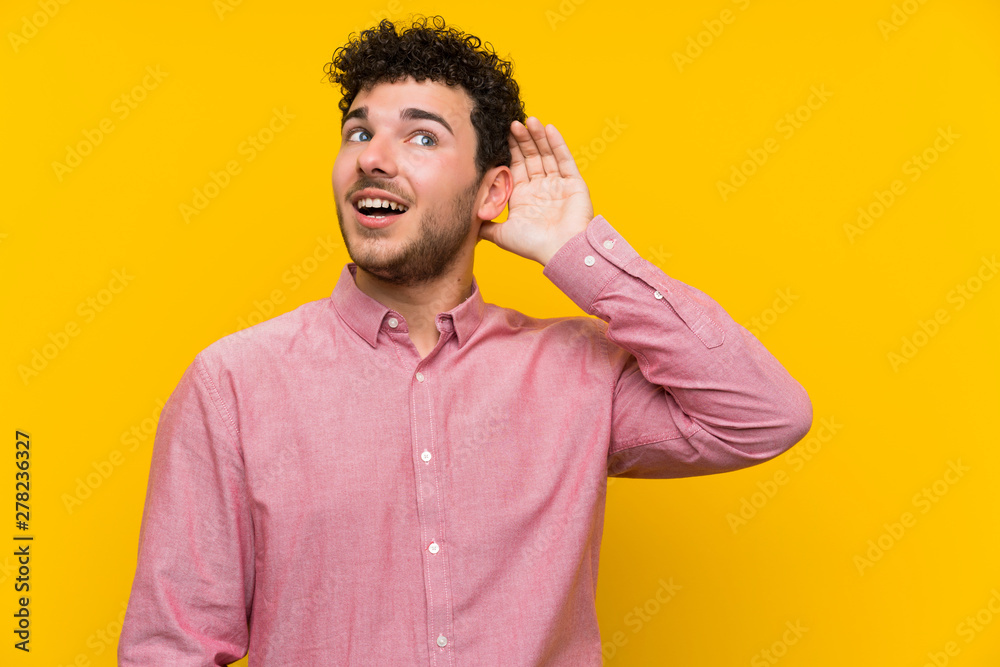 Man with curly hair over isolated yellow wall listening something Man with curly hair over isolated yellow wall listening something