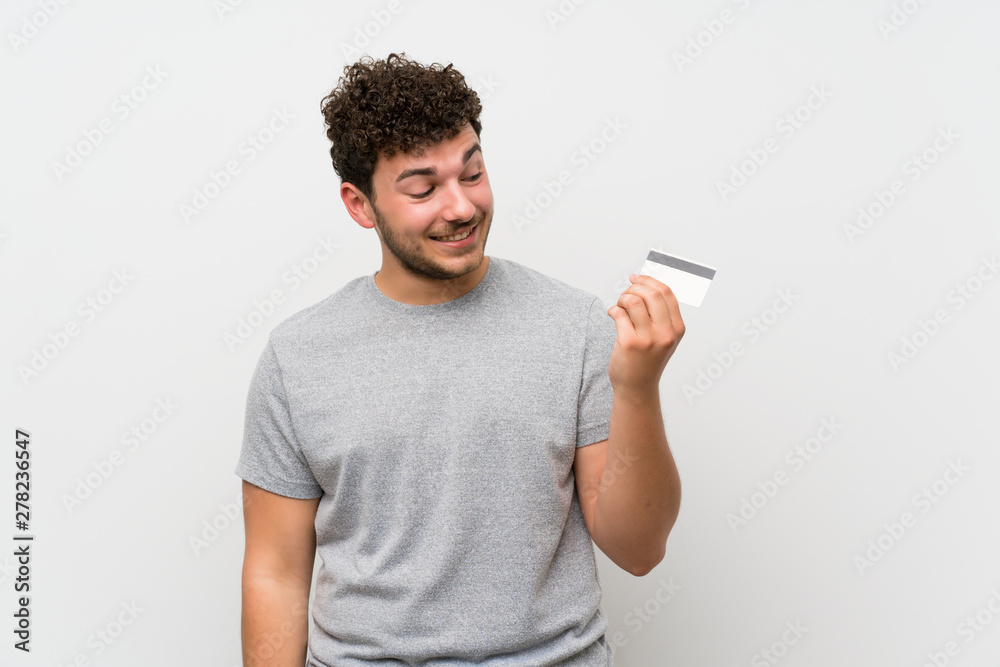 Man with curly hair over isolated wall holding a credit card Man with curly hair over isolated wall holding a credit card