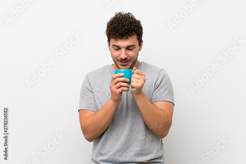 Man with curly hair over isolated wall holding hot cup of coffee