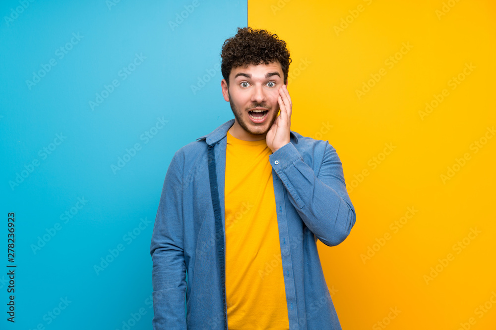 Man with curly hair over colorful wall with surprise and shocked facial expression Man with curly hair over colorful wall with surprise and shocked facial expression