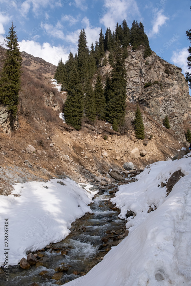 Mountain spring river  with show around and rock mountain on background, Almaty, Kazakhstan
