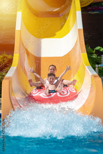 Obraz na płótnie European boy and mom gliding down slide in waterpark. They enjoy the fun and holding hands wide open. w salonie