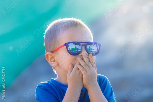 Young white preschool 4 years old boy in sunglasses is surprised or frightened on a sunny summer day photo