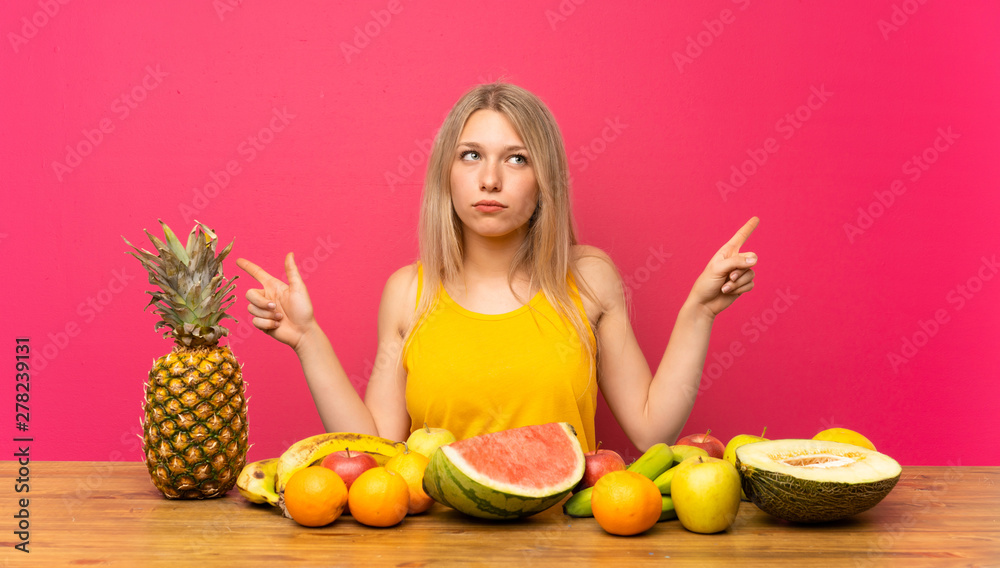 Young blonde woman with lots of fruits pointing to the laterals having doubts Young blonde woman with lots of fruits pointing to the laterals having doubts