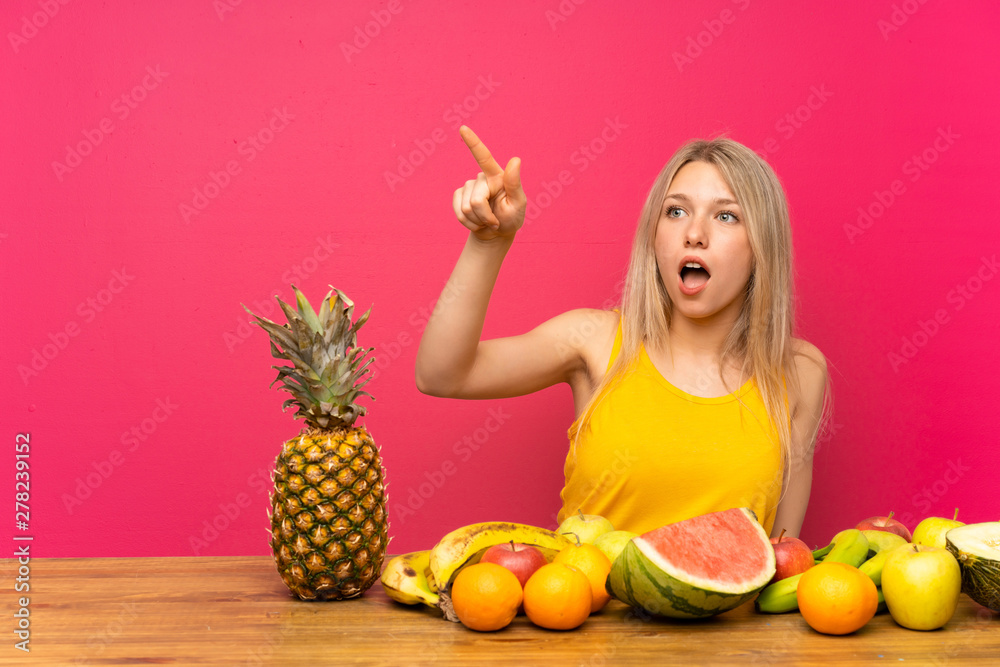Obraz premium Young blonde woman with lots of fruits pointing away