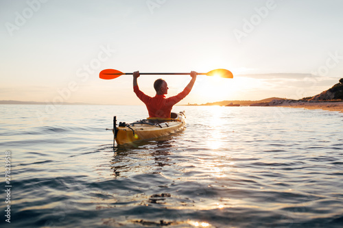 Rear view of man holds kayak paddles high. Active senior in a kayak on the sunset sea 