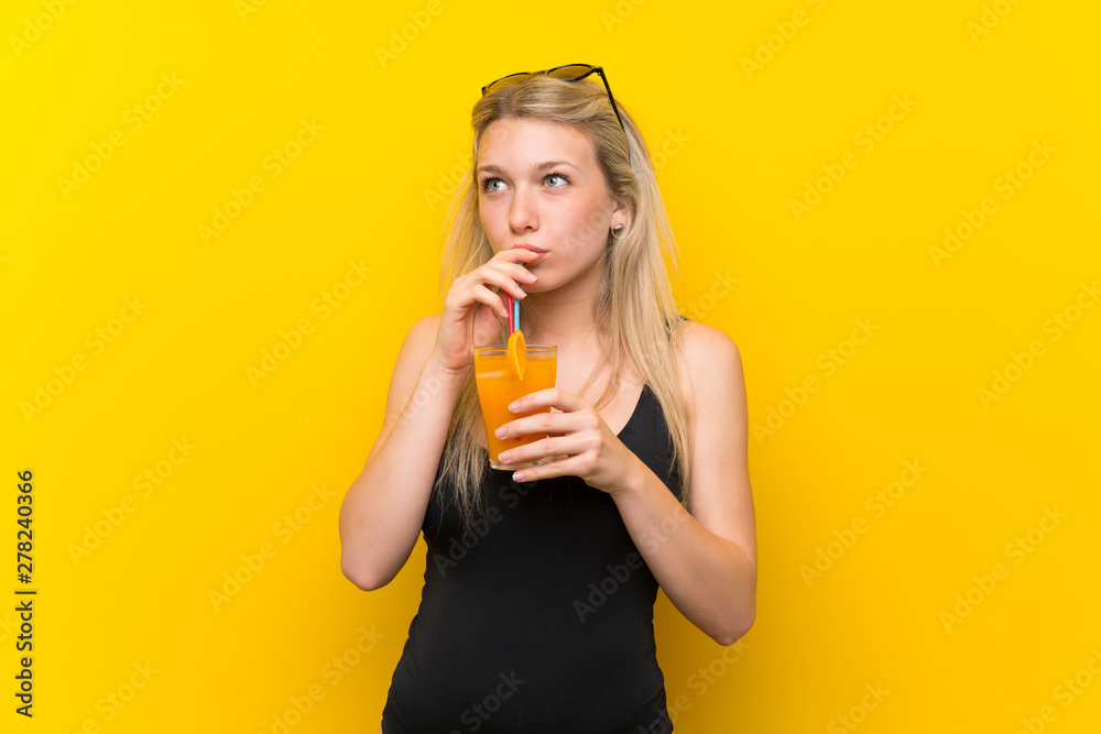 Young woman in swimsuit over yellow background with a cocktail