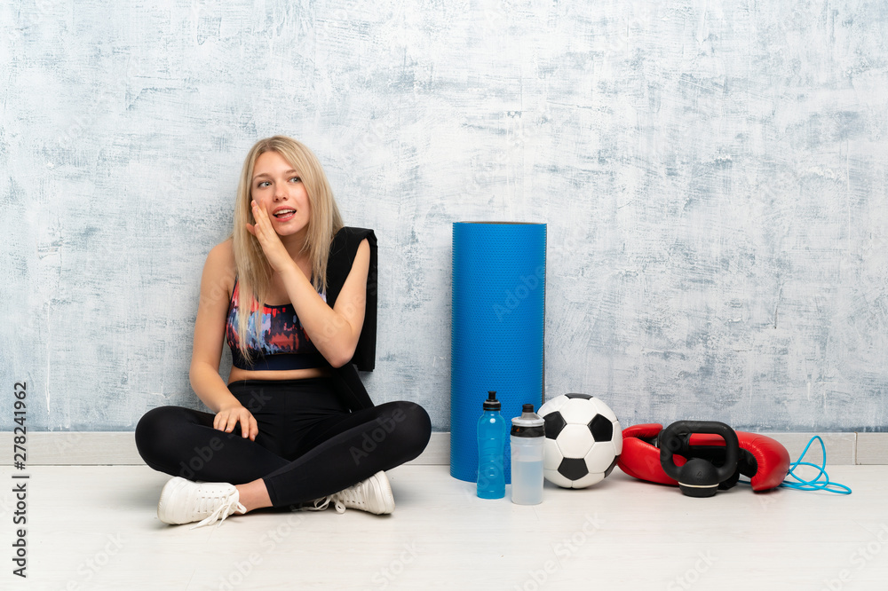 Young blonde sport woman sitting on the floor whispering something