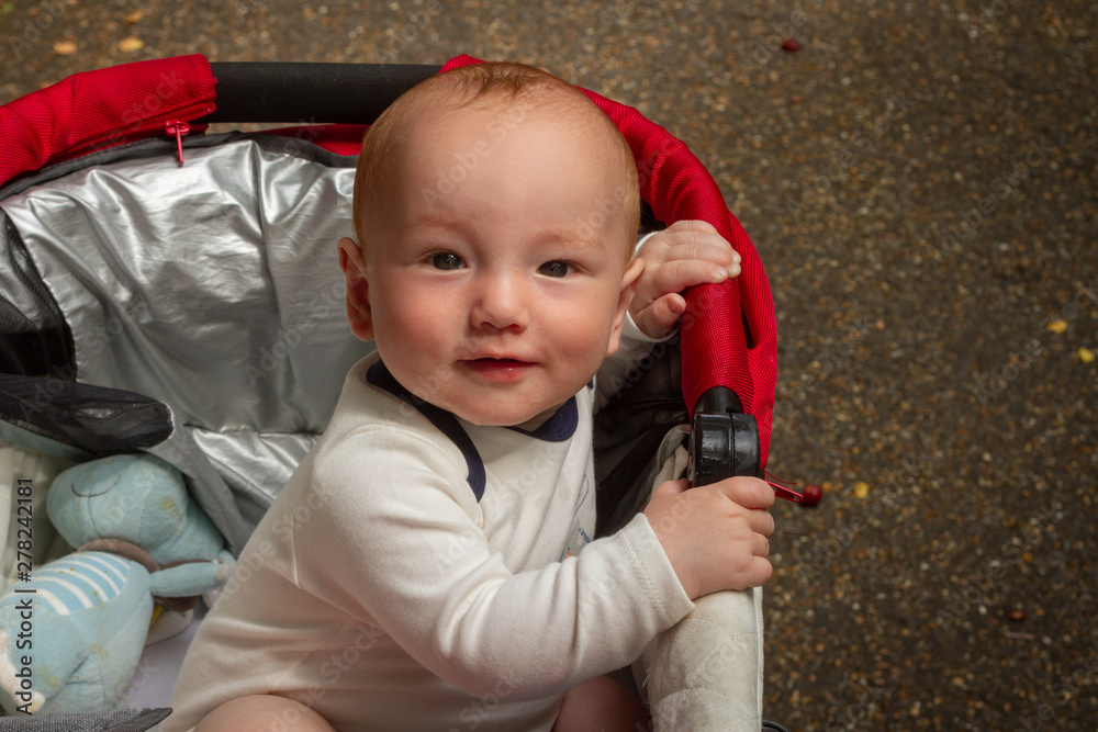 Fototapeta premium Baby holding on the side of buggy or pram top and smiling into the camera