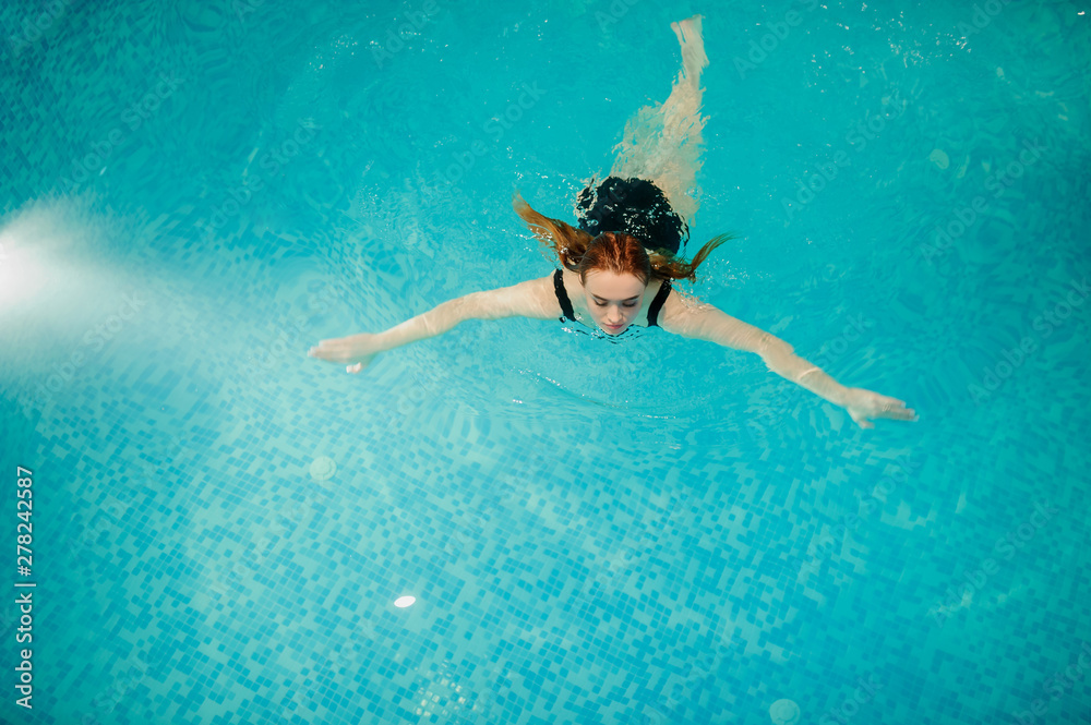 top view of a sexy beautiful reddish woman in black bath costume swimming in the swimming pool of a spa centre